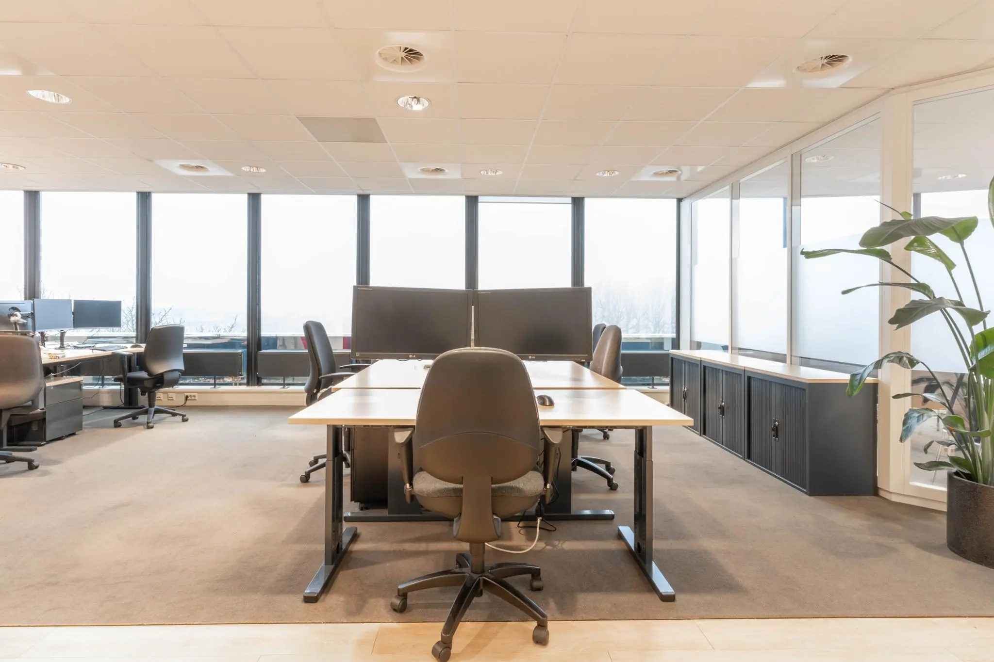 Moderne kantooruimte aan de 1e Hogeweg met bureaus, bureaustoelen, grote ramen en een overzichtelijk interieur.